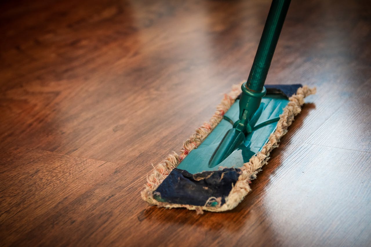 about-us-01 A detailed view of a mop cleaning a wooden floor, showing texture and pattern.